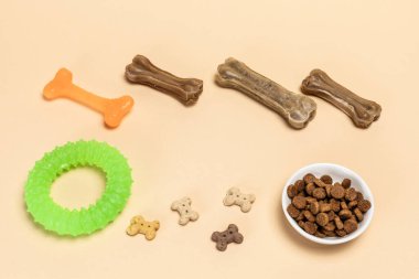 Kuru yiyecek ve köpekler için eğlenceli oyuncaklar. Granüle edilmiş hayvan bir kasede beslenir ve yapay köpek kemik yiyeceğini vitaminlerle çiğner. Kauçuk bir kemik ve bir yüzük. Üst görünüm.