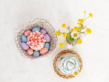 Tatlı Paskalya pastaları, ahşap sepetlerde renkli Paskalya yumurtaları ve beyaz arka planda cam vazoda sarı Ranunculus asiaticus. Üst görünüm.