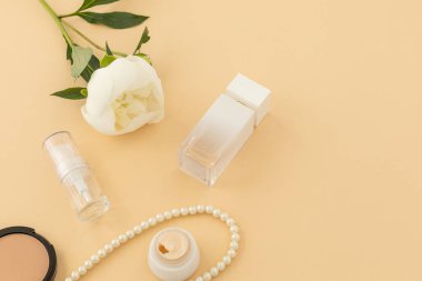Yüz serumu, krem, toz dolu bir kutu, bir şişe parfüm ve bej arkaplanda boncuklar. Kadın kozmetik ve aksesuarları. Üst görünüm.