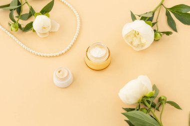 Yüz ve el kremi, bej arka planda beyaz şakayık çiçekli boncuklar. Kadın kozmetik ve aksesuarları. Üst görünüm.