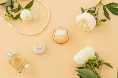 Yüz ve el kremi, bir şişe parfüm ve bej arka planda boncuklar. Kadın kozmetik ve aksesuarları. Üst görünüm.