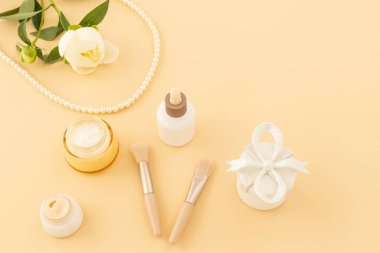 Yüz serumu, yüz ve el kremi, fırçalar, hediye kutusu ve bej arka planda boncuklar. Kadın kozmetik ve aksesuarları. Üst görünüm.
