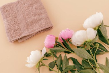 Yüz ve vücut bakımı ürünleri. Beiger arka planında yumuşak terli havlu ve şakayık çiçekleri. Spa ve vücut bakımı seti. Üst görünüm.