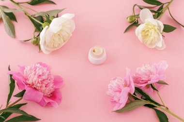 Yüz kremi, pembe arka planda kırmızı ve beyaz şakayık çiçekleri. Kadın kozmetik ürünleri. Üst görünüm.