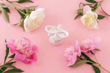 Kadın parfümlü hediye kutusu, pembe arka planda kırmızı ve beyaz şakayık çiçekleri. Üst görünüm.