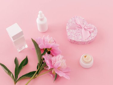 Bir şişe parfüm, yüz kremi, yüz kremi, hediye kutusu ve pembe arka planda şakayık çiçekleri. Kadın kozmetik ürünleri. Üst görünüm.
