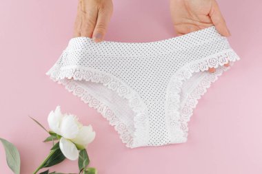 Kadınların elleri pembe arka planda şakayık çiçekli bikinili pamuk külot tutuyor. En iyi günlük iç çamaşırları. Üst görünüm.
