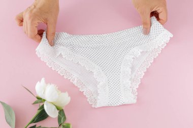 Kadınların elleri pembe arka planda şakayık çiçekli bikinili pamuk külot tutuyor. En iyi günlük iç çamaşırları. Üst görünüm.