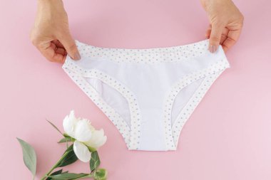 Kadınların elleri pembe arka planda şakayık çiçekli bikinili pamuk külot tutuyor. En iyi günlük iç çamaşırları. Üst görünüm.