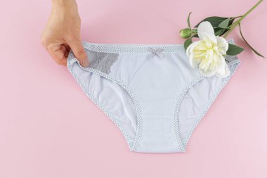 Kadının elinde pembe arka planda şakayık çiçekli bikinili pamuk külot var. En iyi günlük iç çamaşırları. Üst görünüm.
