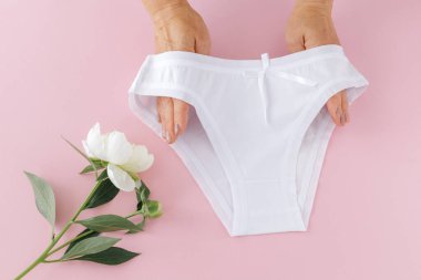 Kadınların elleri pembe arka planda şakayık çiçekli bikinili pamuk külot tutuyor. En iyi günlük iç çamaşırları. Üst görünüm.