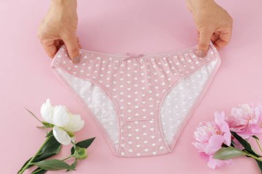 Kadınların elleri pembe arka planda şakayık çiçekli bikinili pamuk külot tutuyor. En iyi günlük iç çamaşırları. Üst görünüm.