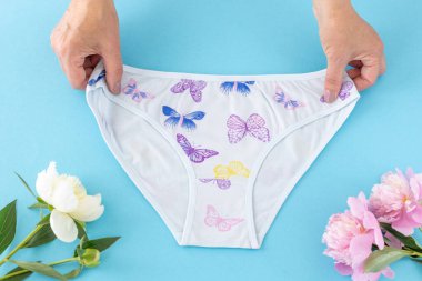 Mavi arka planda şakayık çiçekli, bikinili pamuk külot tutan kadınların elleri. En iyi günlük iç çamaşırları. Üst görünüm.