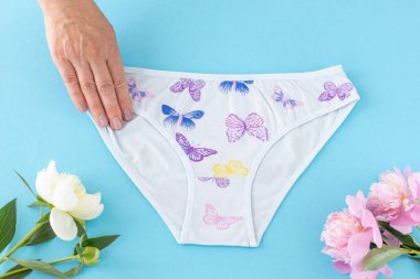 Mavi arka planda, üzerinde şakayık çiçekleri olan bikinili pamuk külot tutan bir kadın eli. En iyi günlük iç çamaşırları. Üst görünüm.