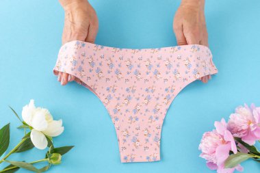 Mavi arka planda şakayık çiçekli minimalist tanga tarzı pamuk külot tutan kadınların elleri. En iyi günlük iç çamaşırları. Üst görünüm.