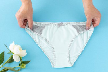 Mavi arka planda şakayık çiçekli, bikinili pamuk külot tutan kadınların elleri. En iyi günlük iç çamaşırları. Üst görünüm.