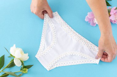 Mavi arka planda şakayık çiçekli, bikinili pamuk külot tutan kadınların elleri. En iyi günlük iç çamaşırları. Üst görünüm.