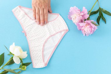 Mavi arka planda, üzerinde şakayık çiçekleri olan bikinili pamuk külot tutan bir kadın eli. En iyi günlük iç çamaşırları. Üst görünüm.