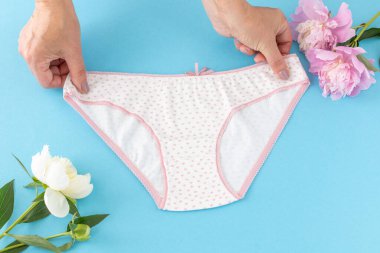Mavi arka planda şakayık çiçekli, bikinili pamuk külot tutan kadınların elleri. En iyi günlük iç çamaşırları. Üst görünüm.