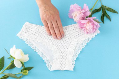 Mavi arka planda dantelli, bikinili pamuk külot tutan bir kadın eli. En iyi günlük iç çamaşırları. Üst görünüm.