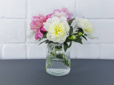 Cam vazoda kırmızı ve sarı şakayıklı çiçeklerden oluşan güzel bir buket ve arka planda beyaz bir duvar var. Kutlama konsepti.