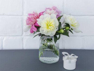 Cam vazoda güzel kırmızı ve sarı şakayık çiçekleri ve arka planda beyaz bir duvar olan hediye kutusu. Kutlama konsepti.