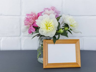 Cam vazoda güzel kırmızı ve sarı şakayık çiçekleri ve fotokopi alanı olan ahşap bir fotoğraf çerçevesi. Kutlama konsepti.