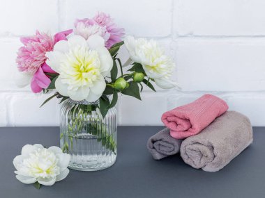 Yüz ve vücut bakımı ürünleri. Yumuşak havlular ve cam vazoda şakayık çiçekleri. Spa ve vücut bakımı seti. Üst görünüm.