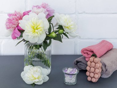 Yüz ve vücut bakımı ürünleri. Yumuşak havlu, sabun, deniz tuzu ve cam vazoda şakayık çiçekleri. Spa ve vücut bakımı seti. Üst görünüm.