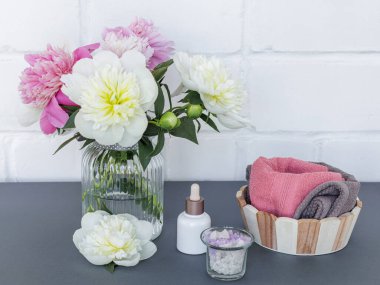 Yüz ve vücut bakımı ürünleri. Bir şişe yüz serumu, deniz tuzu ve ahşap sepetin içinde şakayık çiçekleri olan yumuşak terli havlular. Spa ve vücut bakımı konsepti. Üst görünüm.