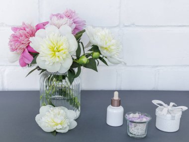 Yüz ve vücut bakımı ürünleri. Bir şişe yüz serumu, deniz tuzu dolu bir kase, bir hediye kutusu ve cam vazoda şakayık çiçekleri. Spa ve vücut bakımı konsepti. Üst görünüm.