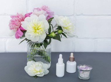 Yüz ve vücut bakımı ürünleri. Yüz serumu şişeleri, cam vazoda deniz tuzu ve şakayık çiçekleri olan bir kase. Spa ve vücut bakımı konsepti. Üst görünüm.