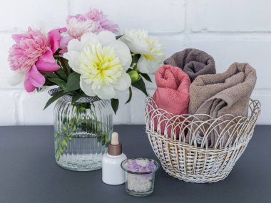 Yüz ve vücut bakımı ürünleri. Bir şişe yüz serumu, deniz tuzu ve sepetinde şakayık çiçekli yumuşak terry havlusu olan bir kase. Spa ve vücut bakımı konsepti. Üst görünüm.