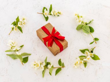 Kırmızı kurdeleli hediye kutusu ve beyaz arka planda güzel yasemin çiçekleri. Üst Manzara. Tatillerde hediye verme kavramı.