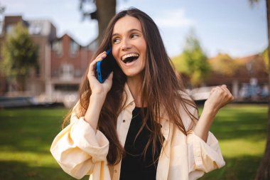 İyi haber dedikoduları. Akıllı telefondaki hoş sohbete şaşırmış mutlu bir kadın dışarıda arkadaşlarıyla konuşmaktan zevk alıyor. Şehir caddesinde yürüyen kız kazandı. Vay canına, iyi haber..