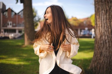 Esmer, mutlu, gülen bir kadın arkadaşlarıyla buluşmaya koşuyor, mutlu görünüyor, gömleğini düzeltiyor, zıplıyor, yan tarafa bakıyor.. 