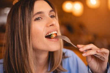Lokantanın içinde çatalla çilek yiyen mutlu kadın yan bakıyor. Sarı saçlı mutlu kızı kapat ve kafede eğlen. Diyet ve taze meyveler.