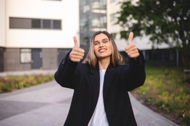 Gömlek ve ceket giymiş, kendine güvenen sarışın bir iş kadınının portresi. Başparmağını göstererek onaylıyor. Güzel bir şey öneriyor..
