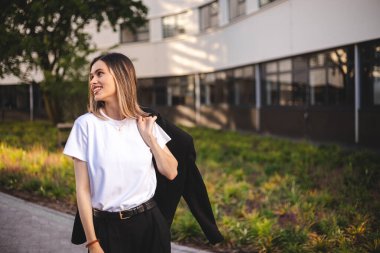 Güzel, kısa saçlı, ceketi omuzunda tutan kadın. Başarılı ve mutlu bir kadın caddede işe gidiyor. Kendine güvenen iş kadını gülümseyerek yürüyor. Mutlu kadın dön ve ceketle yürü.