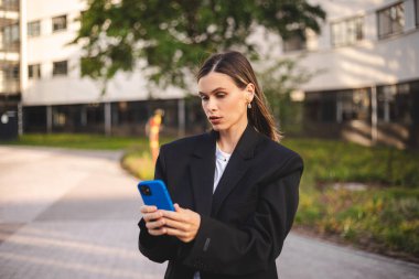 Ciddi düşünceli iş kadını akıllı telefondan mesaj alıyor ve düşünüyor. Elinde cep telefonu olan genç bir kadın ve şüpheli görünüyor. Kız ceketini giyer ve şehrin yakınında durur..