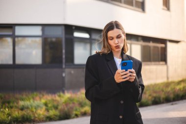 Ciddi düşünceli iş kadını akıllı telefondan mesaj alıyor ve düşünüyor. Elinde cep telefonu olan genç bir kadın ve şüpheli görünüyor. Kız ceketini giyer ve şehrin yakınında durur..