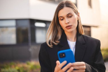 Ciddi düşünceli iş kadını akıllı telefondan mesaj alıyor ve düşünüyor. Elinde cep telefonu olan genç bir kadın ve şüpheli görünüyor. Kız ceketini giyer ve şehrin yakınında durur..