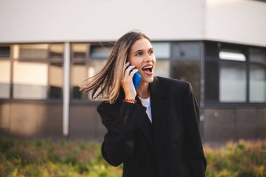 Konuşan mutlu sarışın kadın mutlu, gülümseyen, ağzı açık. İş kadını gülerken cep telefonu konuşması yapıyor. Vay canına, kız siyah ceket giyiyor..
