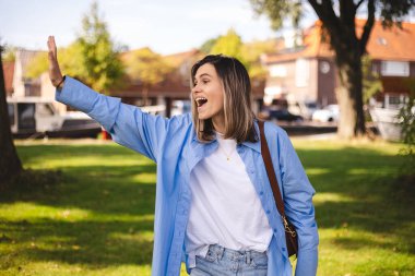 Gülümseyen mutlu kadın, yan el salla, merhaba de, selam ver, heyecanlı. Kız mavi gömlek, beyaz bluz ve kahverengi çanta giyiyor. Şaşırmış bir kadın arkadaşlarıyla tanışır..