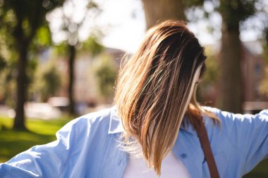 Genç bir kadın güneşli bir günde parkta sakin bir anın tadını çıkarıyor. Sıcak güneş ışığı ve yumuşak odaklı sıradan ve doğal bir yaşam tarzı sahnesi. Parlak saçları ve rahat duruşu huzur ortamı yaratıyor.