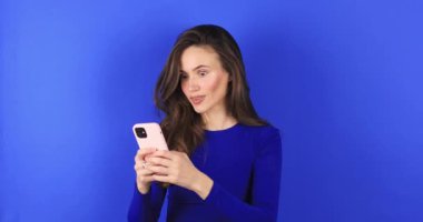 Çekici esmer kadın şaşırmış görünüyor. Vay canına. Mavi arka planda cep telefonu kullanmış. Kız akıllı telefondan birinci sınıf jest yapıyor. Kız az önce büyük galibiyet haberini öğrendi..