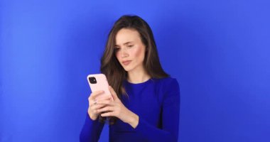 Mad ve şok genç esmer güzel kadın mavi arka planda izole cep telefonu kullanıyor. Bağıran mutsuz kadın cep telefonunu tutuyor. Hayal kırıklığına uğramış üzgün bayan, haberleri dehşete düşürdü. Bu da ne? Olamaz.