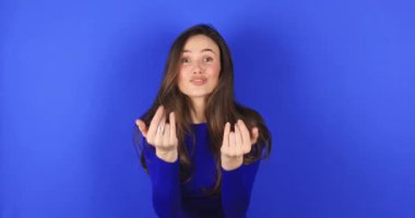 Kollarıma gel. Mavi uzun kollu kahverengi saçlı sevimli kız buraya bedava sarılmak ve mavi arka planda izole edilmiş hoş bir yüz ifadesiyle gülümsemek için geliyor. Bana gel.!