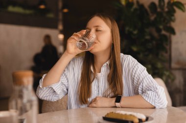 Lokantada oturup bir bardak su içen güzel bir kız. Yemek, eğlence ve insan konsepti. Sarı saçlı kadın soyunmuş gömlek giyiyor..
