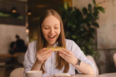Genç sarışın kadın kafede oturmuş ekkin yiyor. Lokantada ekini kıran kız çok neşeli görünüyor. Yemek günü konseptini aldatmak. Kadın ekkin yemek için iştahla hazırlanıyor. Fıstık fırınının tadını çıkar.